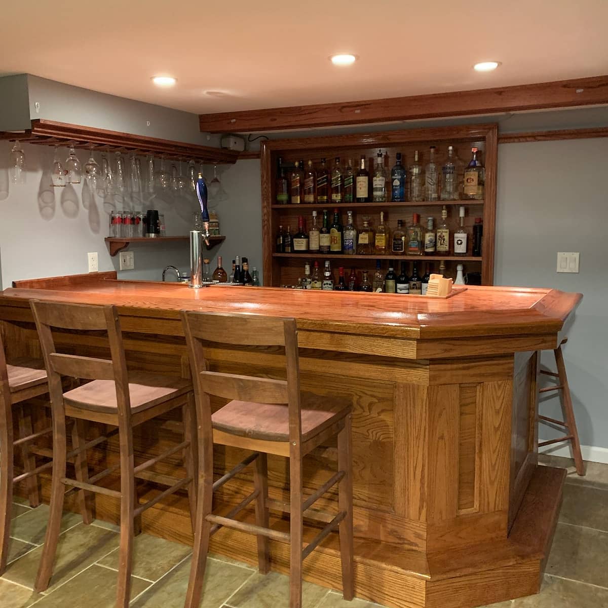 Traditional wooden basement bar with stools, liquor shelves, and hanging glassware.